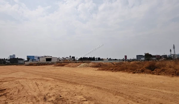 View across the prepared terrain at Sobha One World showing distant site offices, construction hoarding, and the surrounding city skyline indicating its prime location.