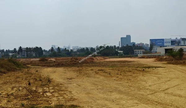 Looking across the wide cleared expanse of the Sobha One World staging area towards commercial billboards and the dense city horizon.